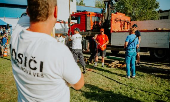 A group of firefighters in a park setting during a public demonstration near a fire truck.
